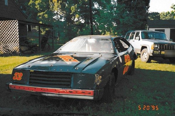 A dark stock car with a big orange 32 on the nose and the door, parked on the grass beside a house. The camera's date stamp reads 5 20 95.