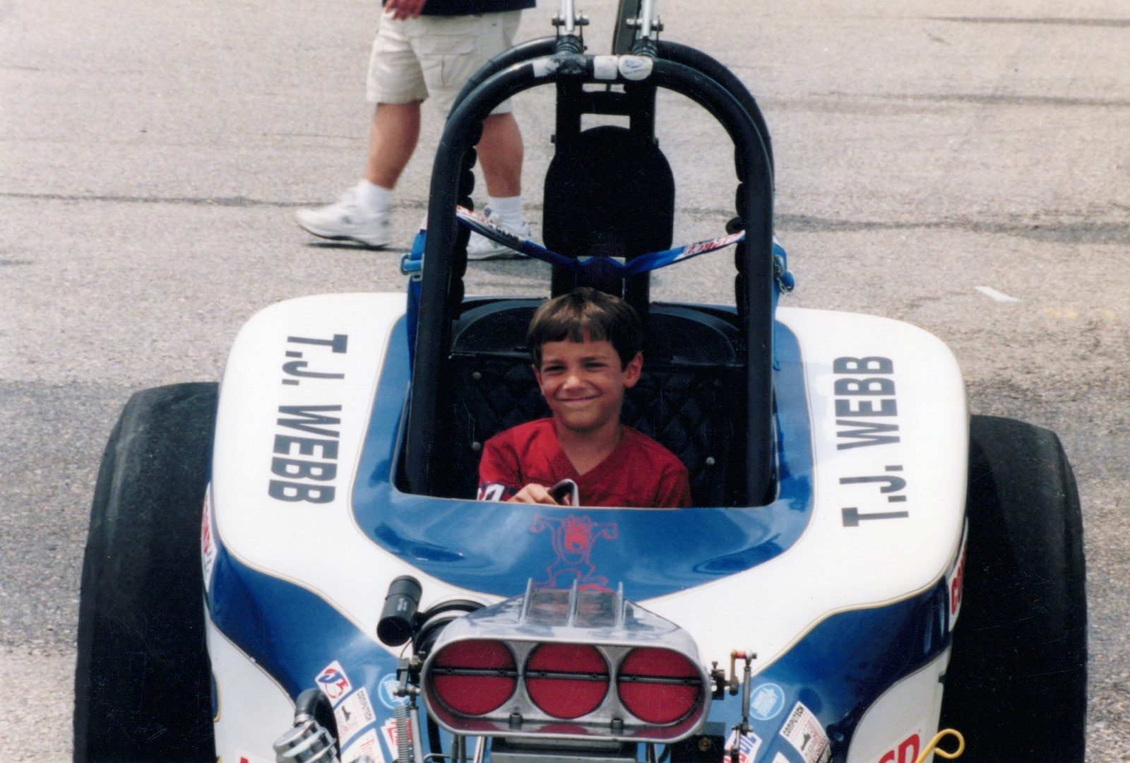Young Chuck grinning in the cockpit of a blue and white dragster.