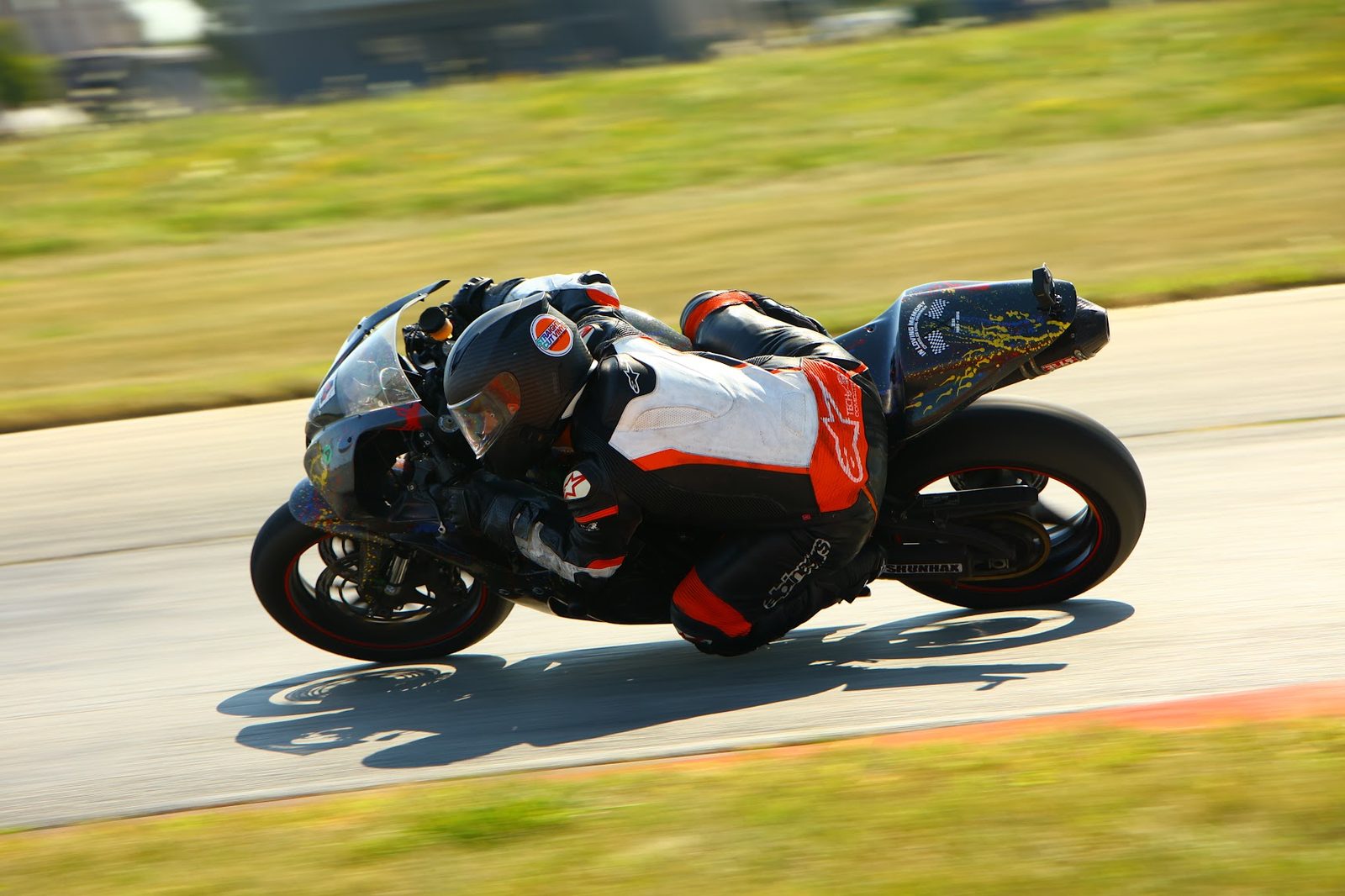 Chuck leaning the splatter-painted race bike into a corner. On the tail, between two checkered flags, is the In Loving Memory sticker for his dad.