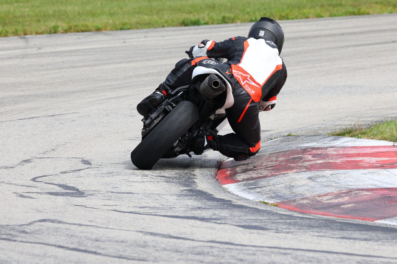 Chuck seen from behind, knee at the red and white kerb, leaning the white race bike into a corner at Autobahn South.