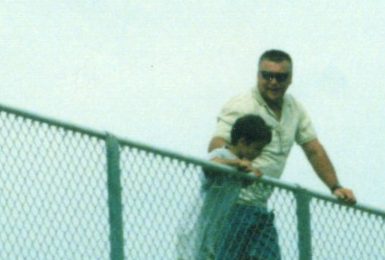 Chuck's dad at the top rail of a grandstand, holding young Chuck up so he can see over it.